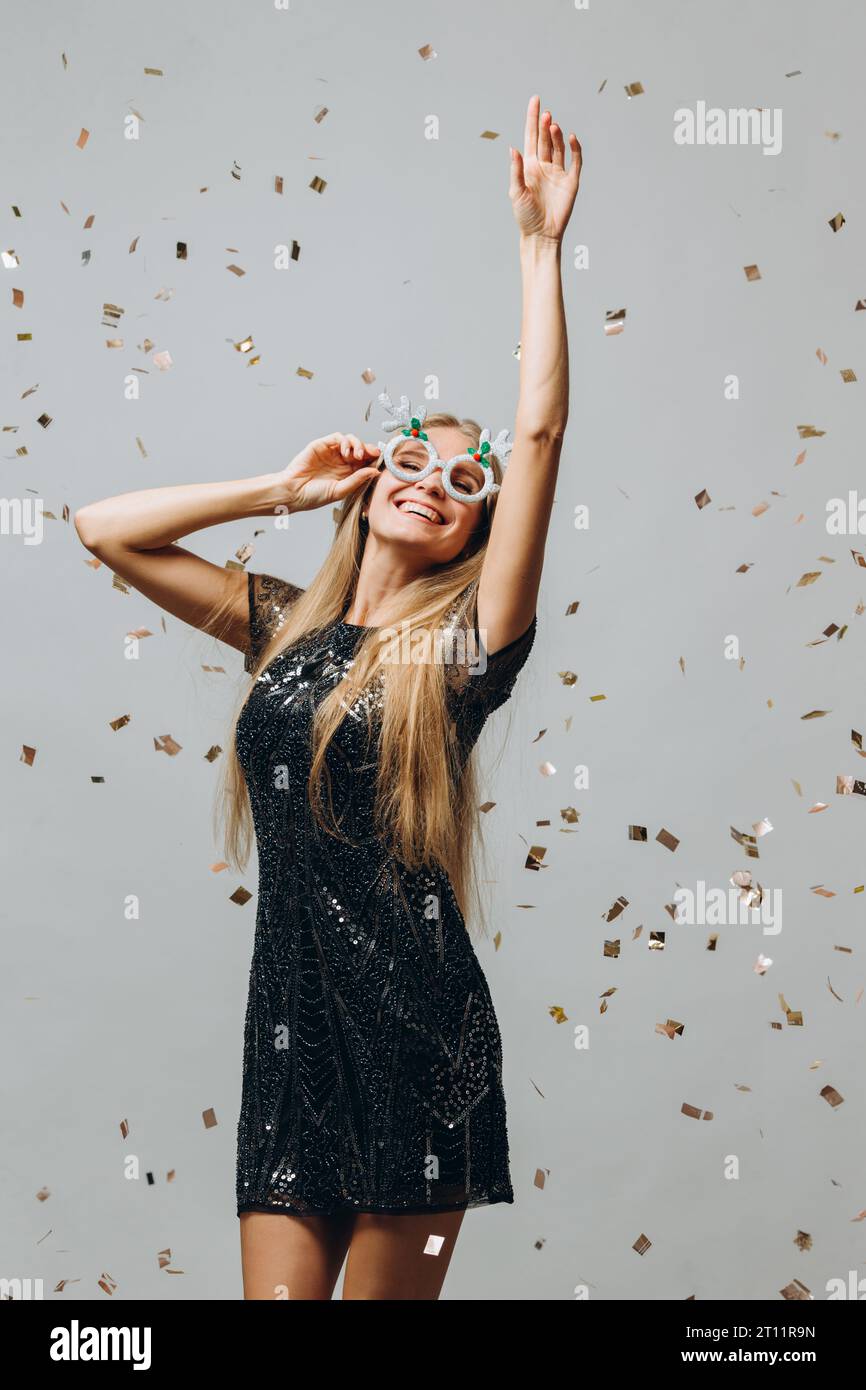 Ein hübsches blondes Mädchen tanzt unter glitzerndem Konfetti. Neujahrsfest-Konzept. Stockfoto