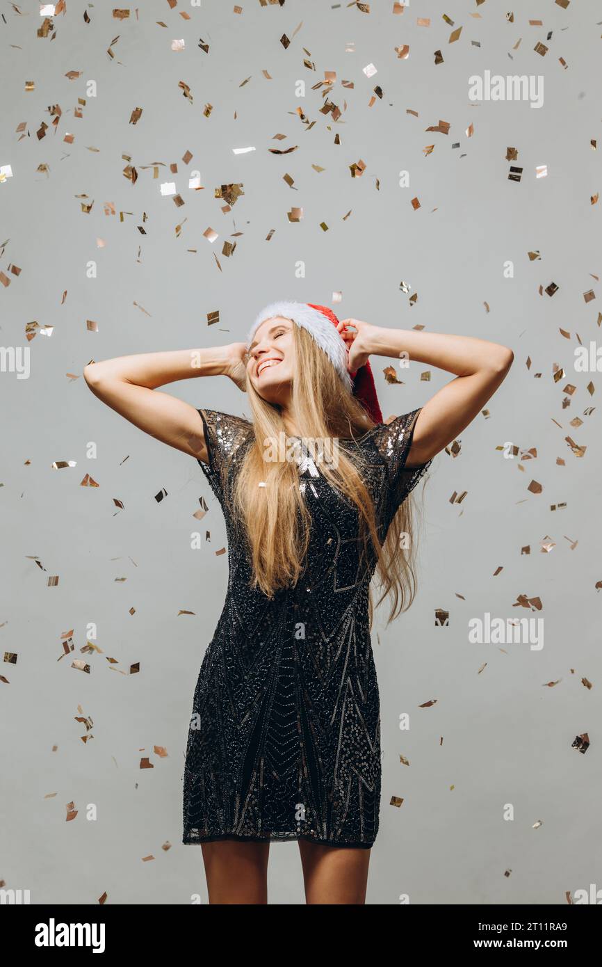 Wunderschönes blondes Weihnachtsmann-Mädchen, das unter glitzerndem Konfetti tanzt. Neujahrsfest-Konzept. Stockfoto