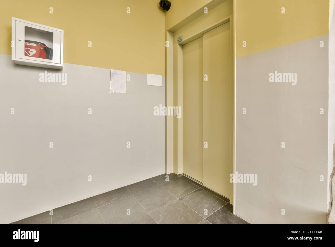 Ein Raum mit gelben Wänden und grauem Boden, einschließlich einer weißen wandmontierten Klimaanlage auf der rechten Seite Stockfoto