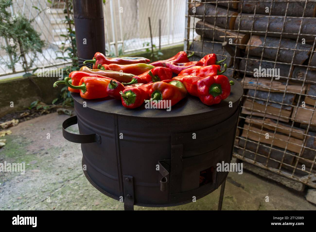 Ein runder Holzofen mit frischen roten Paprika, ordentlich angeordnet, bereit zum Braten im Hof an einem Herbsttag Stockfoto