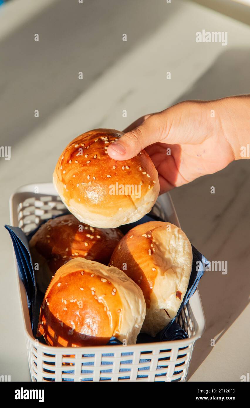 Menschliche Hand hält frisches Burgerbrot. Eine Menge Burger in einem Korb Stockfoto