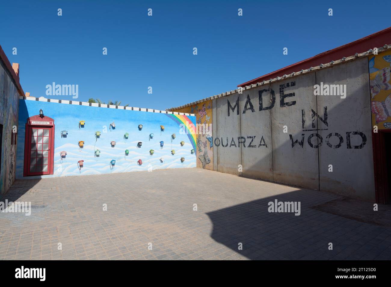 Ouarzazate, Marokko - 10. Oktober 2023: Regenbogenmalte Wand und eine englische Telefonzelle und viele alte Telefone hangen in verschiedenen Farben am Atlas Stockfoto