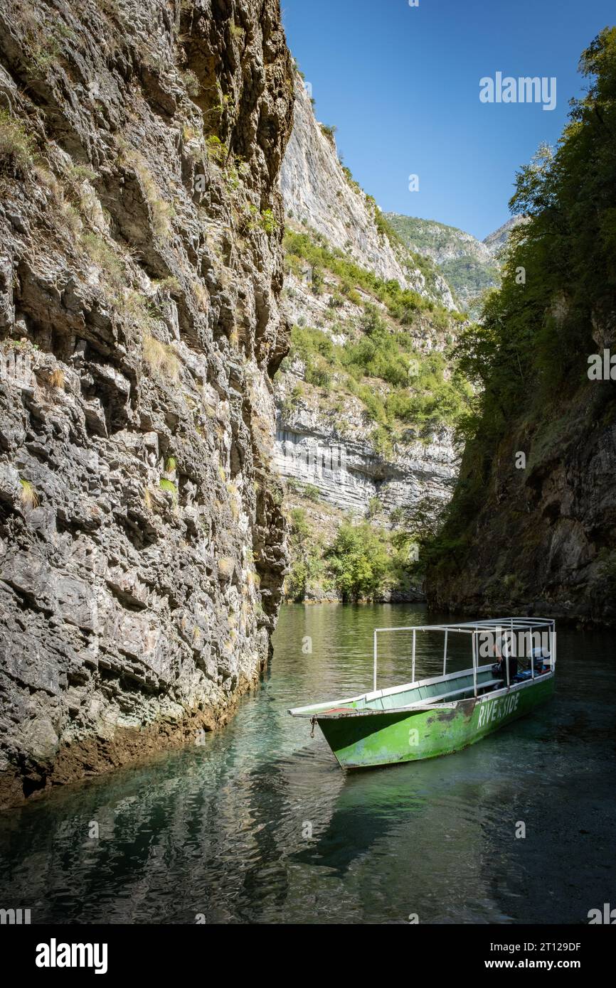 Ein langes, dünnes Ausflugsboot, das an einer steilen Felswände im River Shala Resort im Komani-See, Albanien, verankert ist Stockfoto