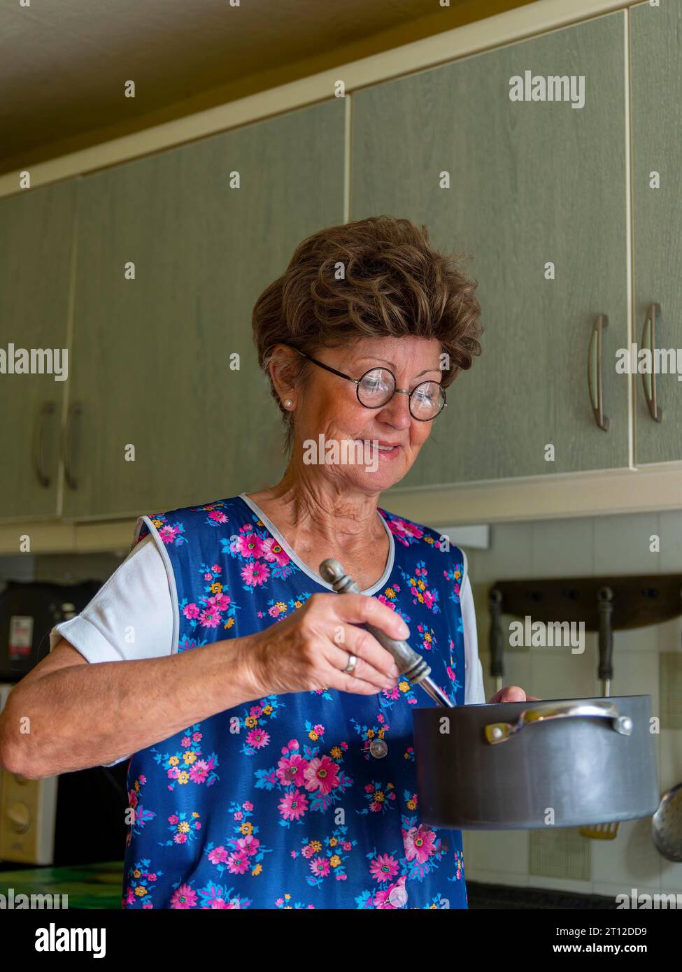 Oma mit alter Kittelschürze, Brille und Perücke in der Küche, hält