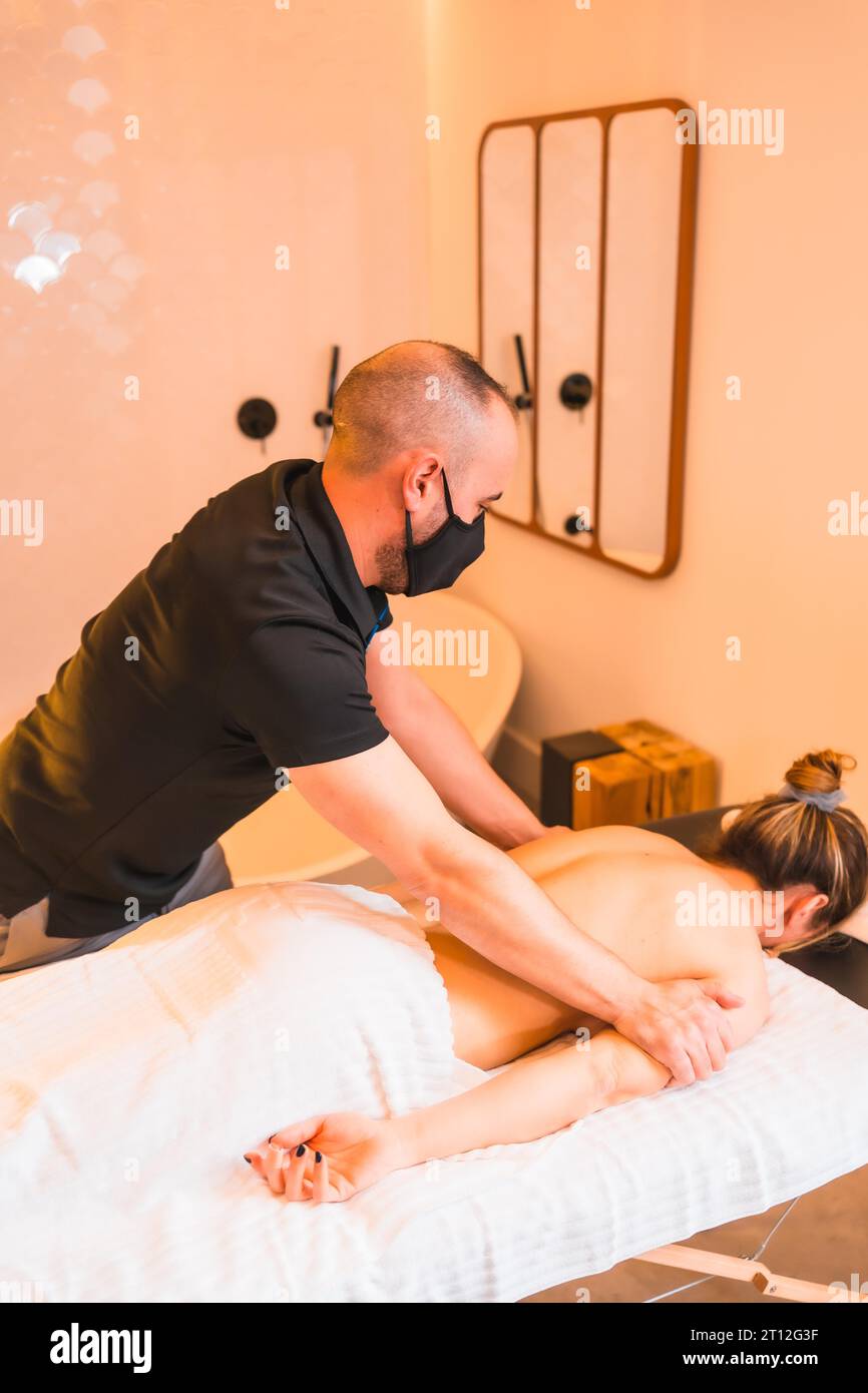 Hausmassage, Massage beim Kunden zu Hause, vertikale Fotos. Mit einer Gesichtsmaske bei der Coronavirus-Pandemie Stockfoto
