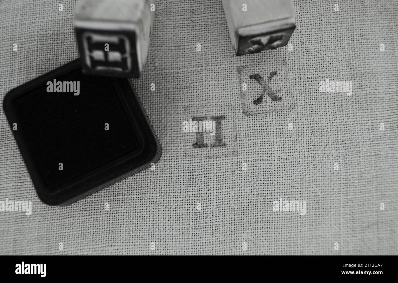 Stempelbuchstaben auf Leinengewebe H und X. Holzstempel und schwarze Stempeltinte. Stockfoto