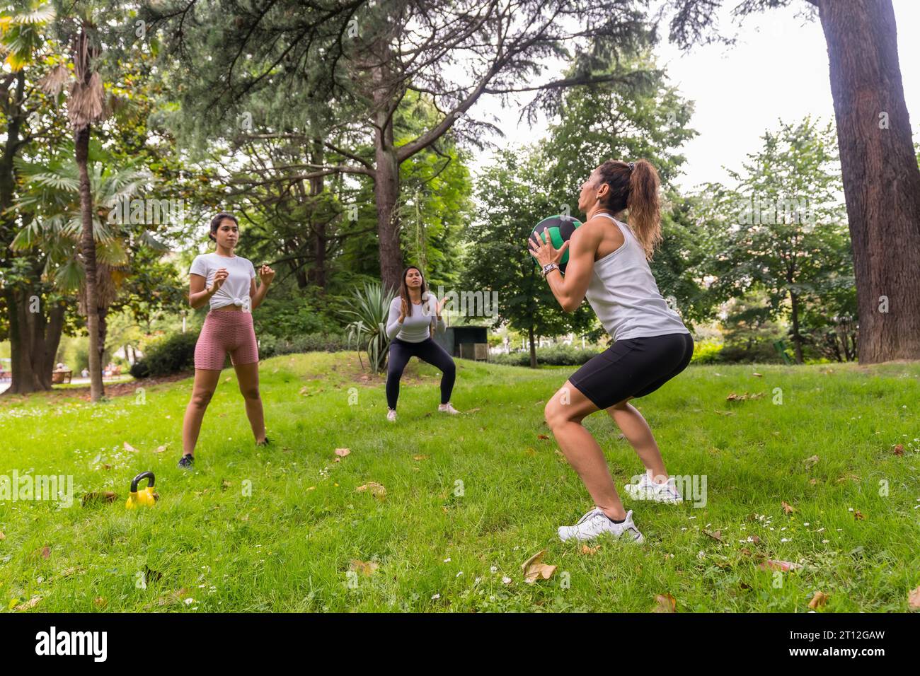 Lateinisches Mädchen, das in einem grünen Park Sport und Bewegung macht, Lehrer unterrichtet die Schüler mit Übungen der Gewichte und einem schweren Ball Stockfoto