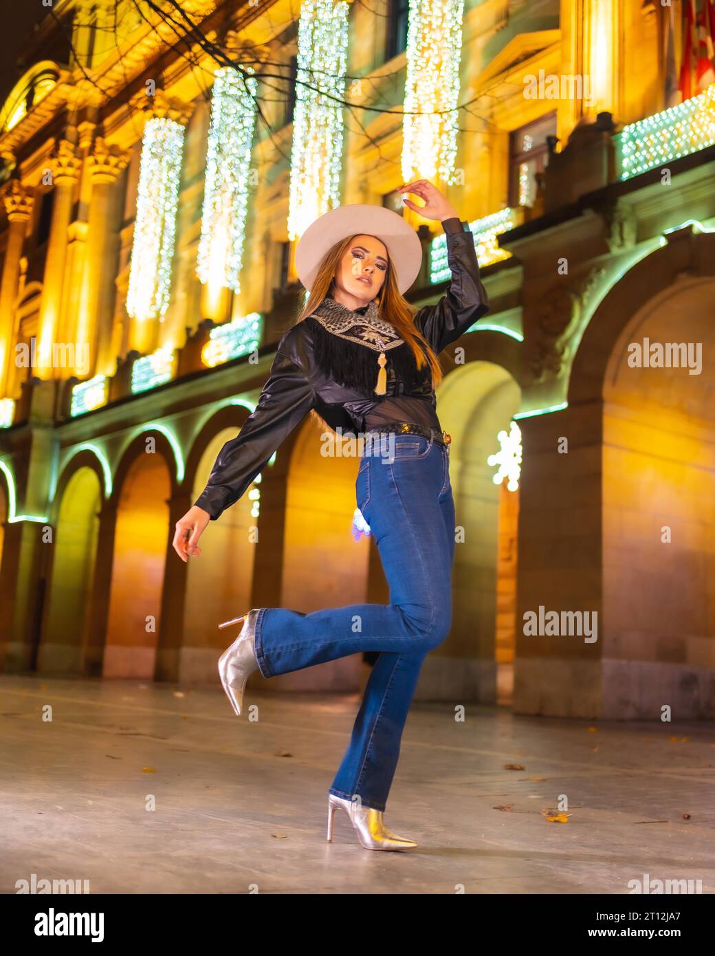 Winterstil, junges weißes blondes Model mit Jeans und schwarzer Jacke in der Stadt, die nachts zu weihnachten beleuchtet wird Stockfoto