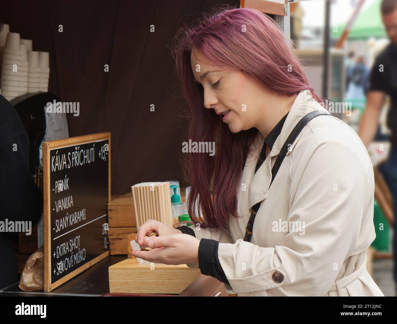 Hübsche junge Frau, die Kaffee kauft und Münzen für Verkäufer am Bauernstand auf dem Straßenmarkt in Prag zählt. Stockfoto