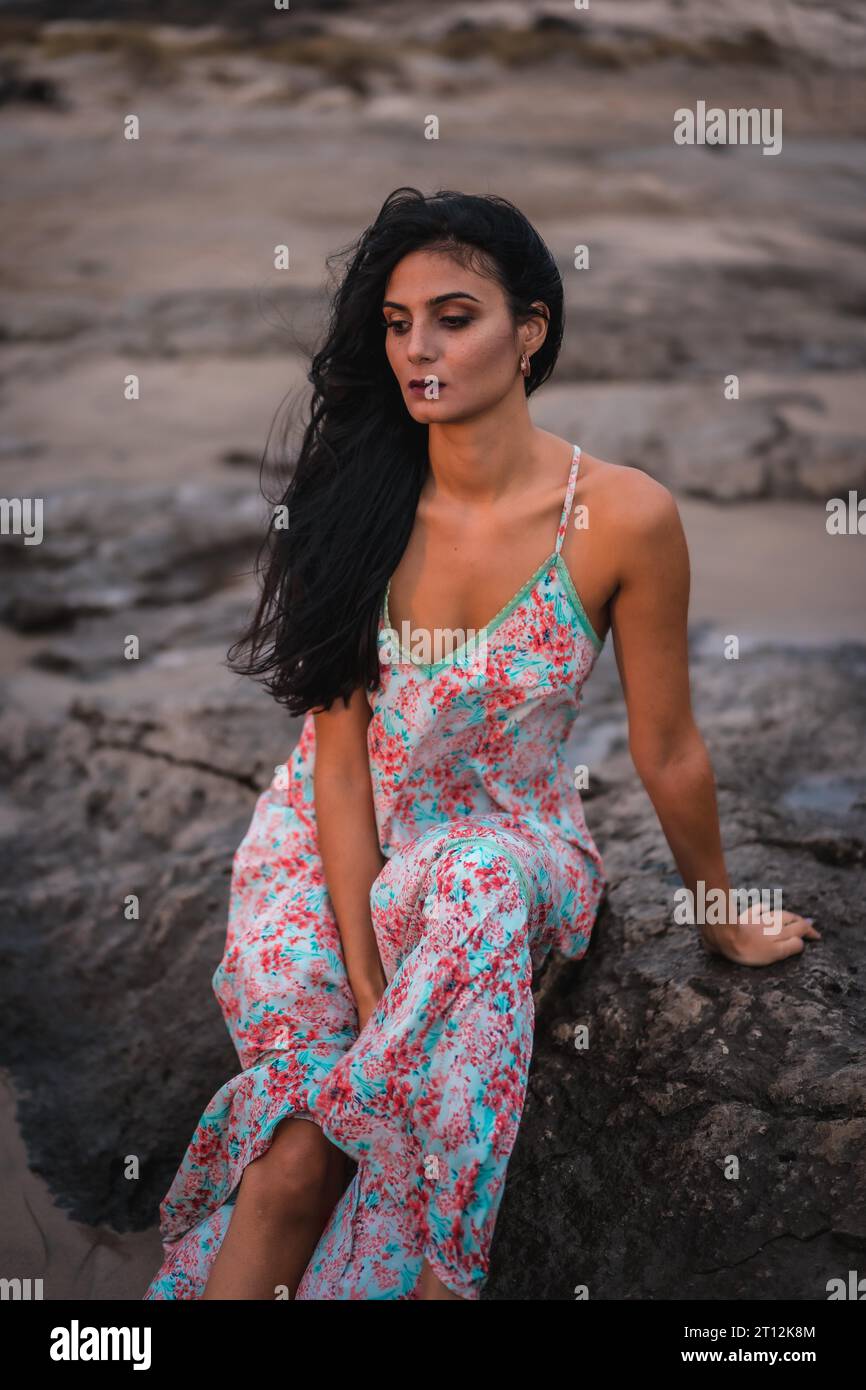 Weißliche Brünette in einem weißen Stoffkleid mit Blumen, am Strand genießen Sie den Urlaub am Meer, vertikales Foto Stockfoto