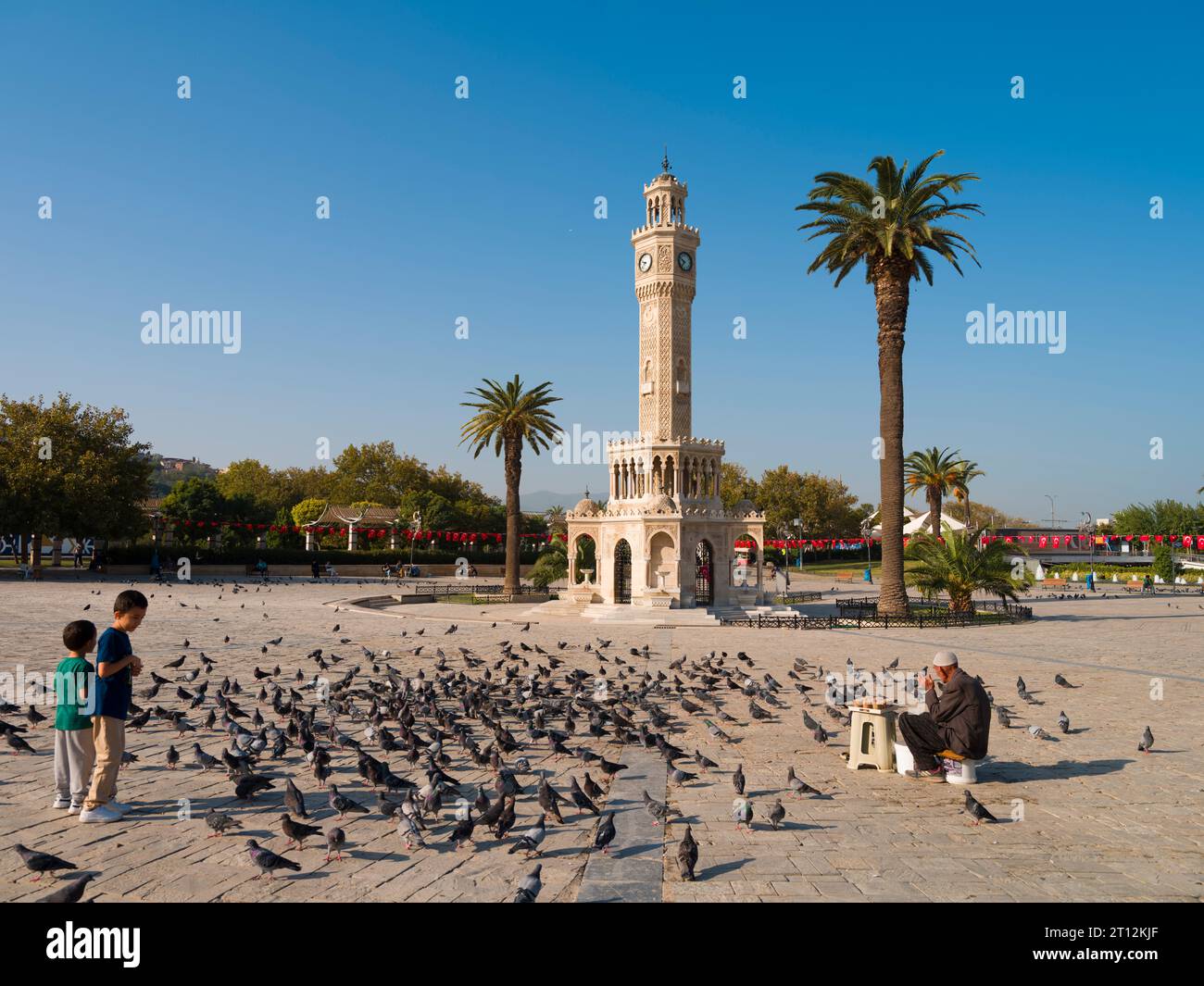 Izmir, Türkei. 5. Oktober 2023. Uhrenturm von Izmir. Taubenfutterverkäufer und Kinder, die mit Tauben spielen. Herbst in Izmir Stockfoto