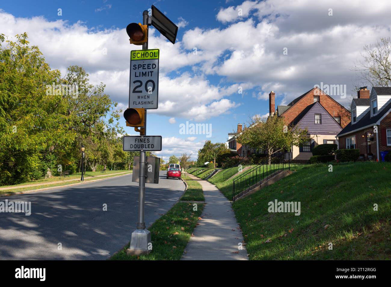 Eine ruhige Vorstadtstraße in Frederick, MD, mit zweistöckigen Häusern, grünen Rasenflächen und einem Warnschild für die Schulzone, das bei 20 km/h blinkt Stockfoto