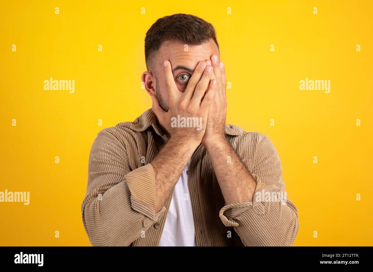 Schockierter tausendjähriger europäer, bedeckt Gesicht mit Händen, Blick von den Fingern Stockfoto