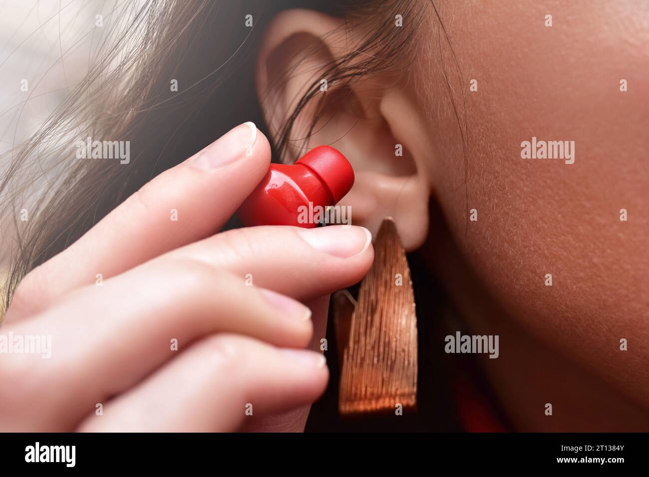 Eine Frau hält einen roten, kabellosen Kopfhörer in der Hand und bringt ihn näher an ihr Ohr, um Musik zu hören. Nahansicht Stockfoto