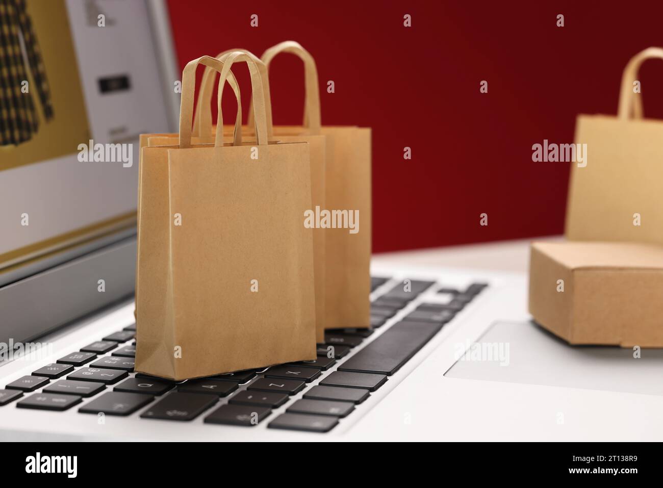 Mini-Einkaufstaschen auf Laptop vor rotem Hintergrund, Nahaufnahme. Online-Shop Stockfoto