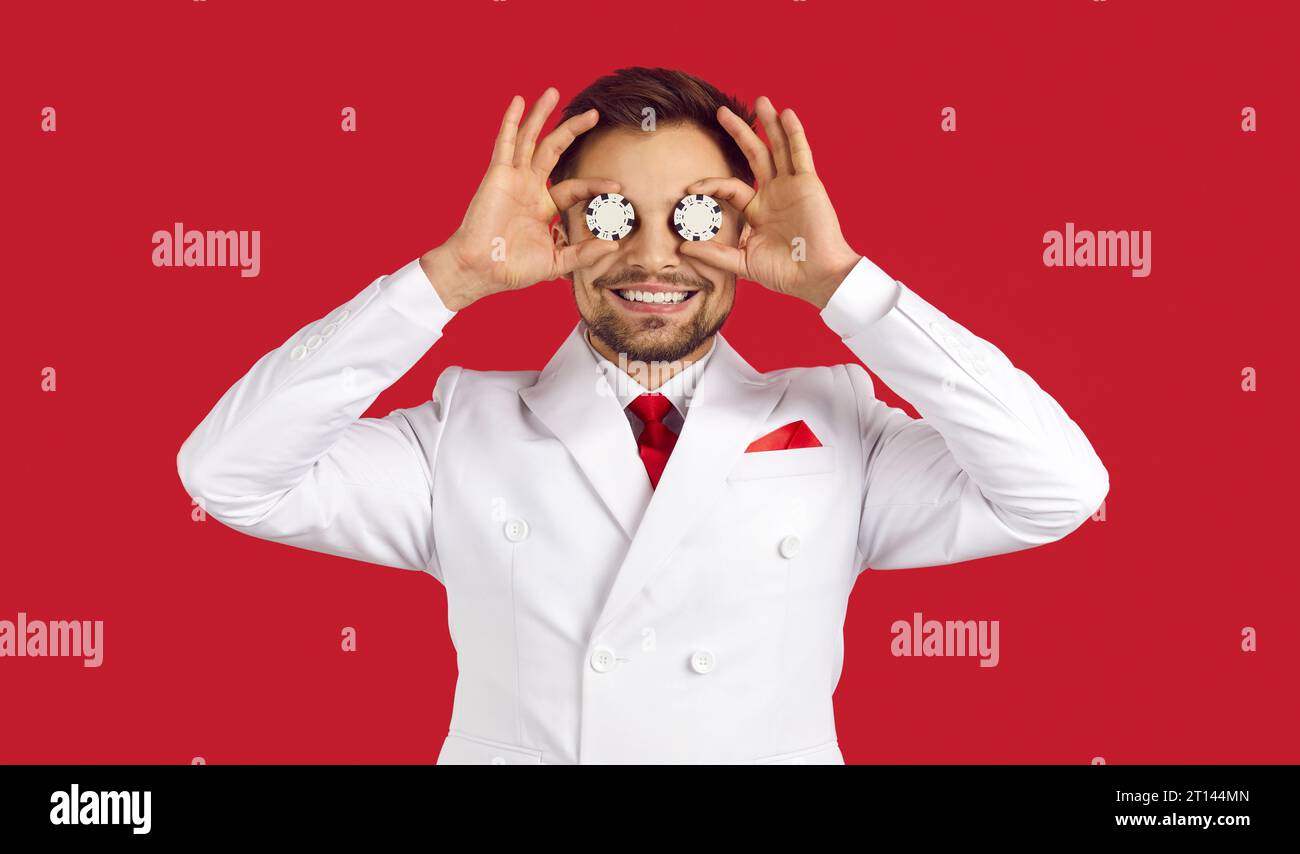 Porträt eines glücklichen jungen Pokerspielers, der Chips auf den Augen hält und lächelt Stockfoto