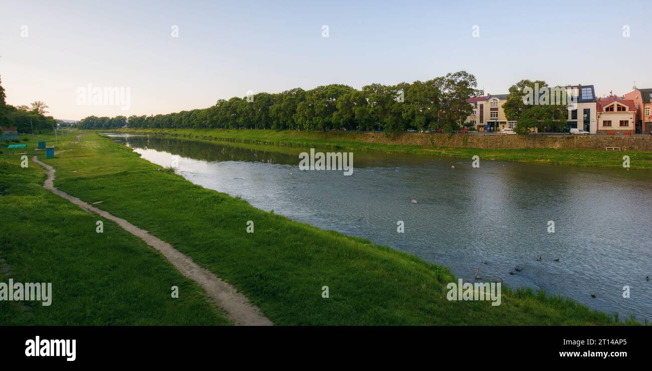 Stadtbild mit Fluss uzh. Ufer der Innenstadt mit alten Gebäuden am anderen Ufer in der Ferne. Sonniger Sommermorgen Stockfoto