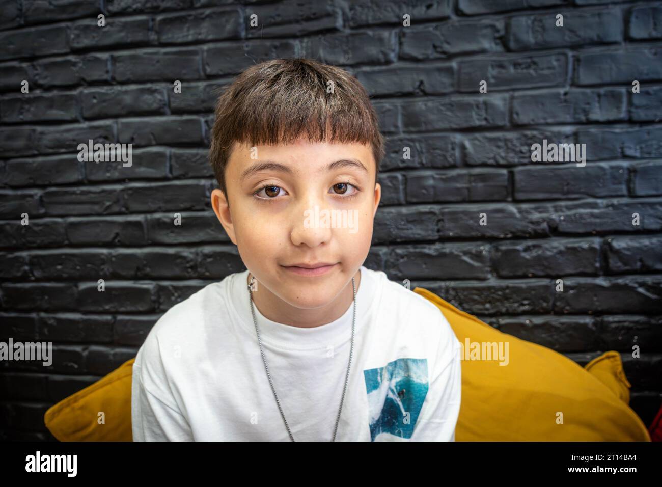 Porträt eines 10-jährigen Jungen mit einer schwarz bemalten Ziegelwand dahinter. Stockfoto
