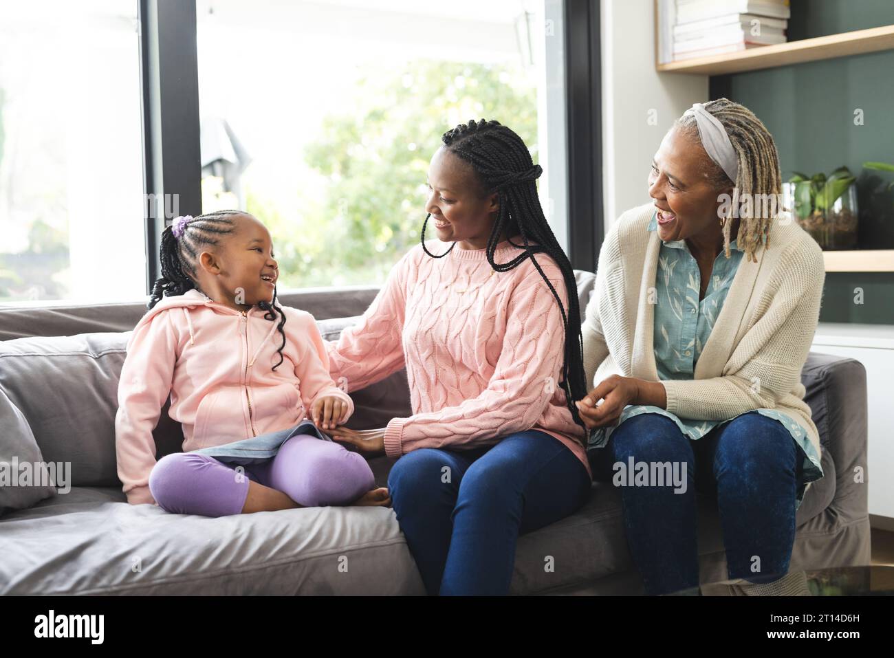 Glückliche afroamerikanische Seniorenmutter, Erwachsene Tochter und Tochter sitzen auf der Couch und reden Stockfoto