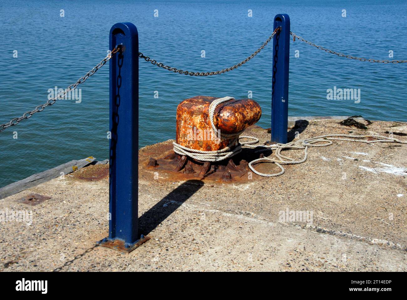 Großer Schiffspoller mit Seil um ihn herum und zwei blauen Metallpfosten am Ende des Betonstegs, Whitstable, Kent Stockfoto