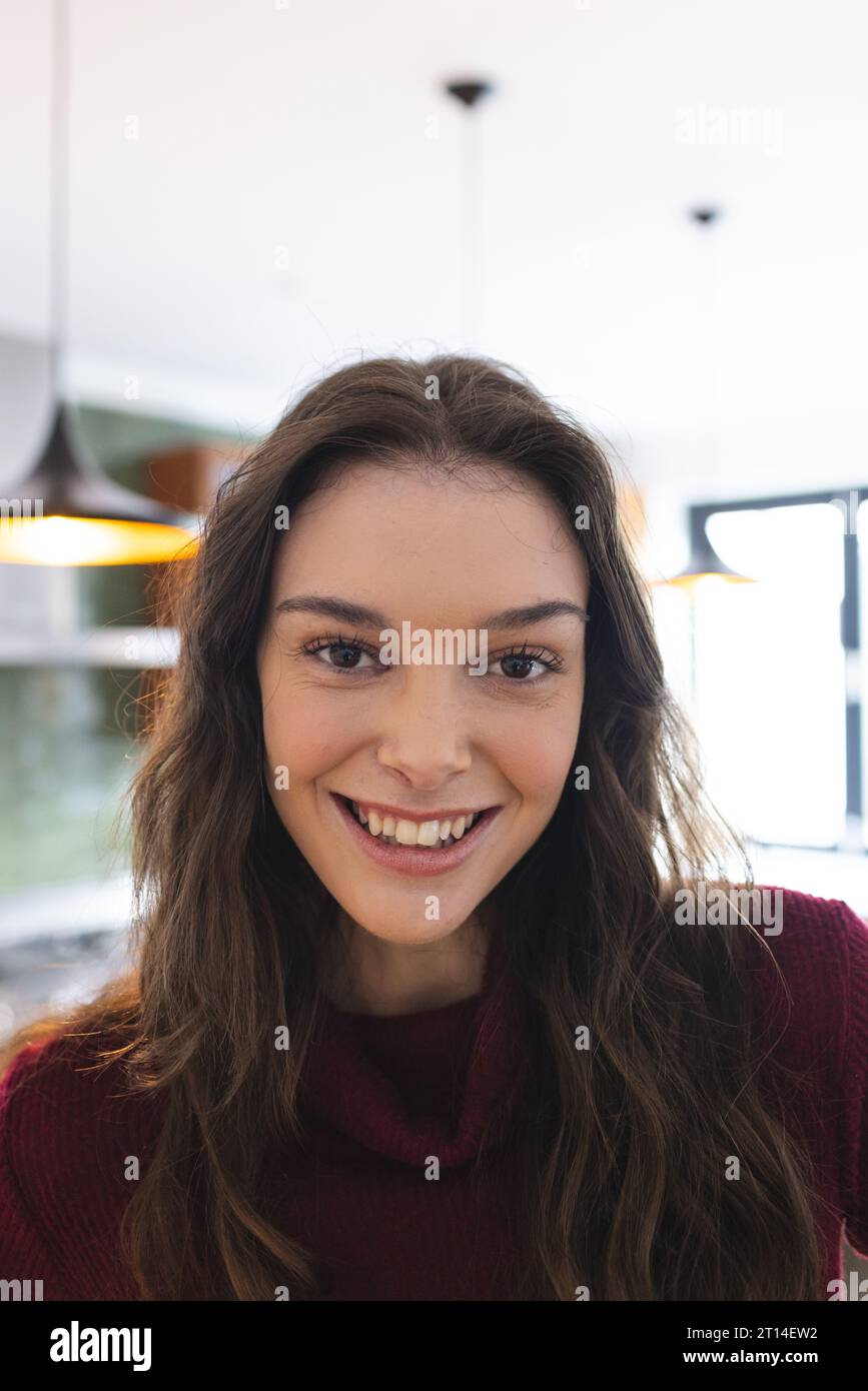 Porträt einer glücklichen kaukasischen Frau mit langen braunen Haaren, die in der Küche zu Hause lächelt Stockfoto