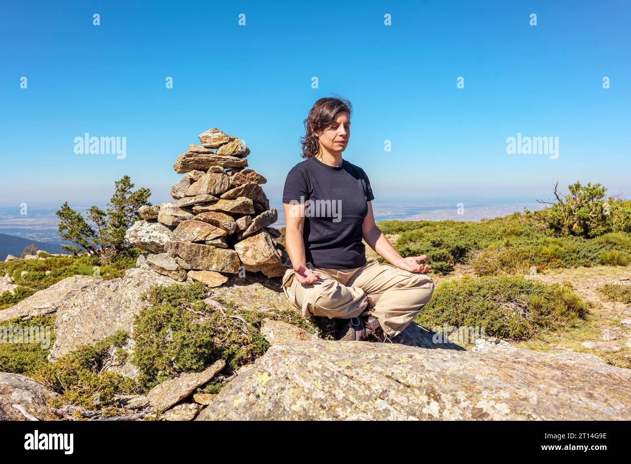 kaukasische Frau mittleren Alters, die neben einem Meilenstein sitzt, in leichter Position für eine Meditationsübung inmitten der Natur. Stockfoto