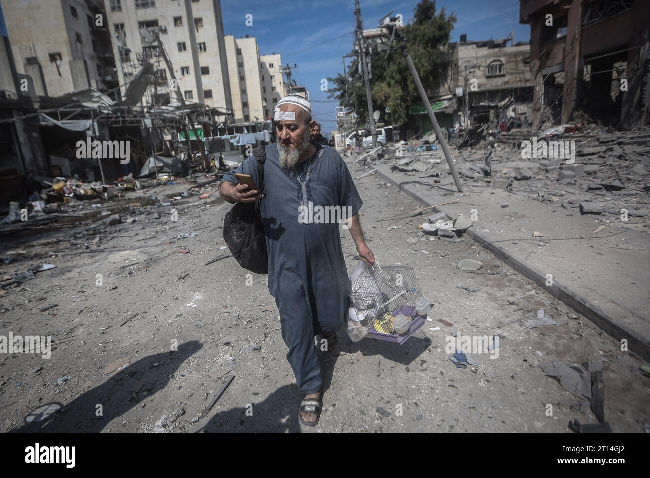 Gaza-Stadt, Palästinensische Gebiete. Oktober 2023. Ein Palästinenser läuft mit seinen Hausvögeln durch eine verwüstete Straße nach dem israelischen Bombenanschlag auf das Viertel Karama in Gaza-Stadt. Quelle: Mohammed Talatene/dpa/Alamy Live News Stockfoto