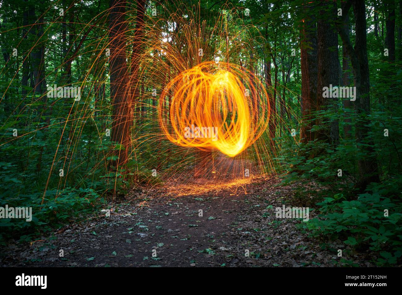 Brennende Stahlwolle, die sich im Wald verspinnt. Nächtliche Schauer von leuchtenden Funken aus spinnender Stahlwolle. Stockfoto