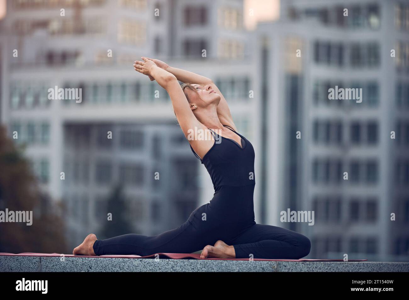 Schöne junge Frau praktiziert Yoga Asana eine beinige Königstaube Pose - Eka Pada Rajakapotasana im Freien vor dem Hintergrund einer modernen Stadt. Stockfoto