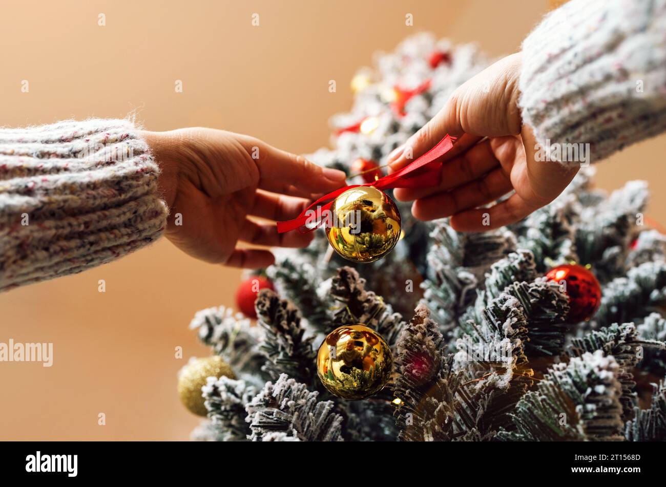 Goldene Kugel und rote Schleife Weihnachtsbaumdekoration in weiblichen Händen Nahaufnahme. Den Weihnachtsbaum schmücken. Stockfoto
