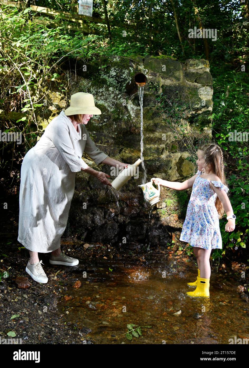 Frau und Kind sammeln frisches Quellwasser aus der Wasserleitung der Mine, angeblich reines Wasser, Spout Lane, Benthall, Shropshire Stockfoto