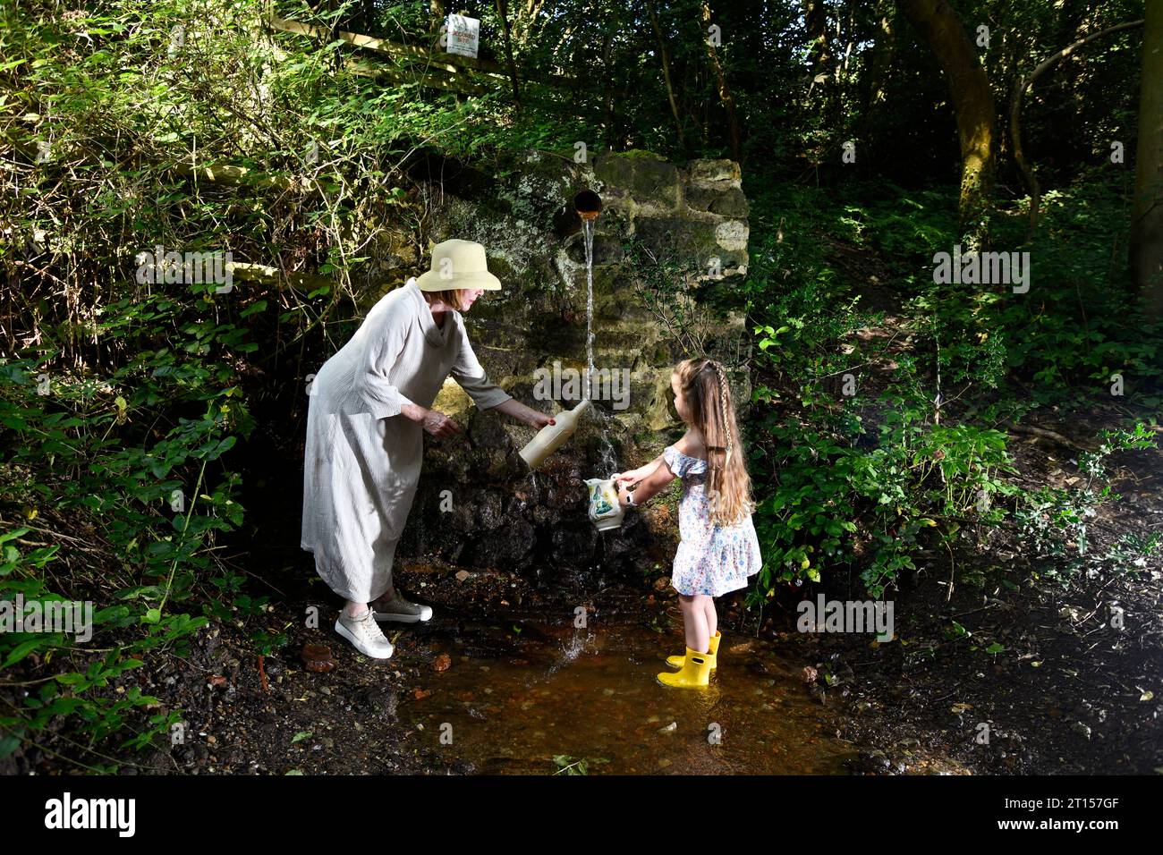 Frau und Kind sammeln frisches Quellwasser aus der Wasserleitung der Mine, angeblich reines Wasser, Spout Lane, Benthall, Shropshire Stockfoto