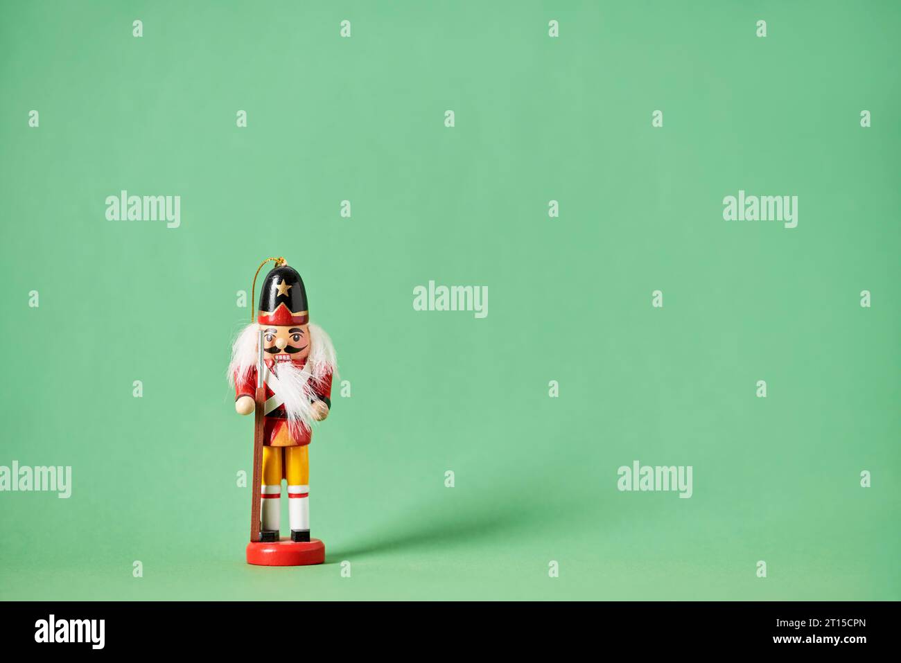 Traditioneller bunter hölzerner Weihnachtsnussknacker in rotem und gelbem Anzug mit grünem Hintergrund, minimaler Komposition mit Kopierraum. Stockfoto