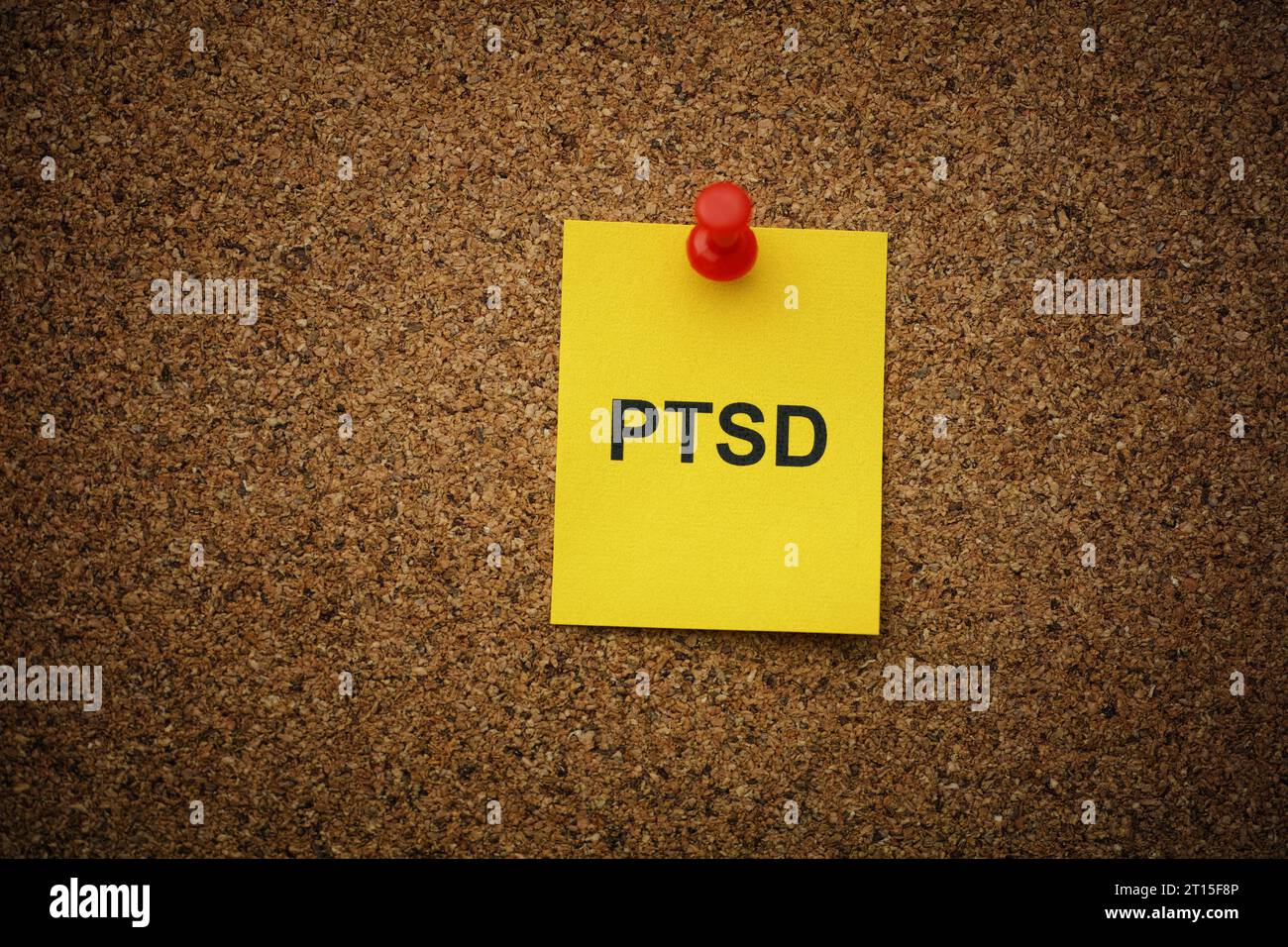 Eine gelbe Papiernote mit der Abkürzung PTSD (posttraumatische Belastungsstörung) darauf, auf eine Korkplatte gesteckt. Nahaufnahme. Stockfoto