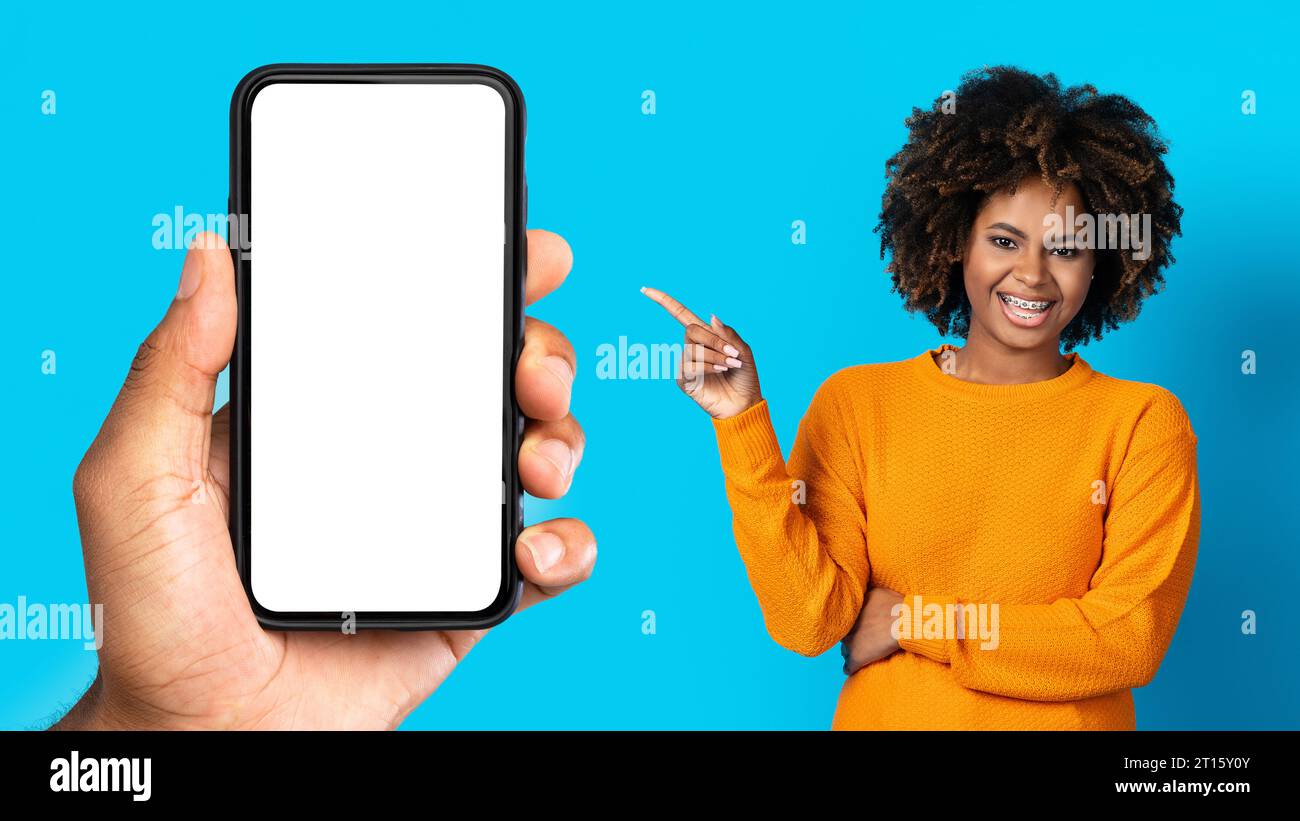 Lächelnde, lockige tausendjährige afroamerikanerin mit Zahnspangen, die mit dem Finger zur Hand zeigt Stockfoto