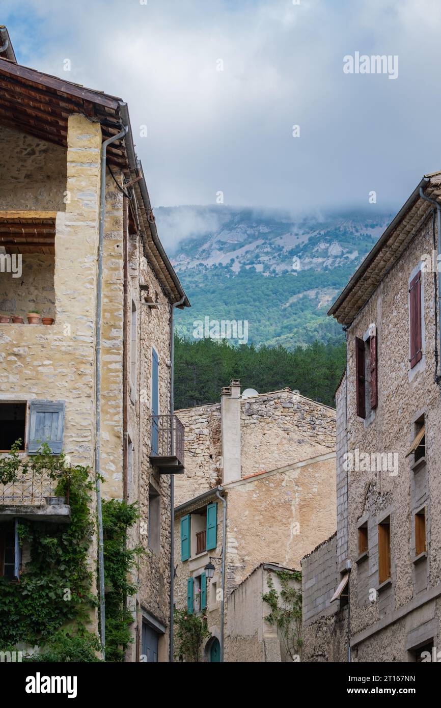 Straßen- und mittelalterliche Häuserfassaden im Dorf Chatillon en Diois mit dem verborgenen Berg hinter Wolken im Hintergrund. Stockfoto