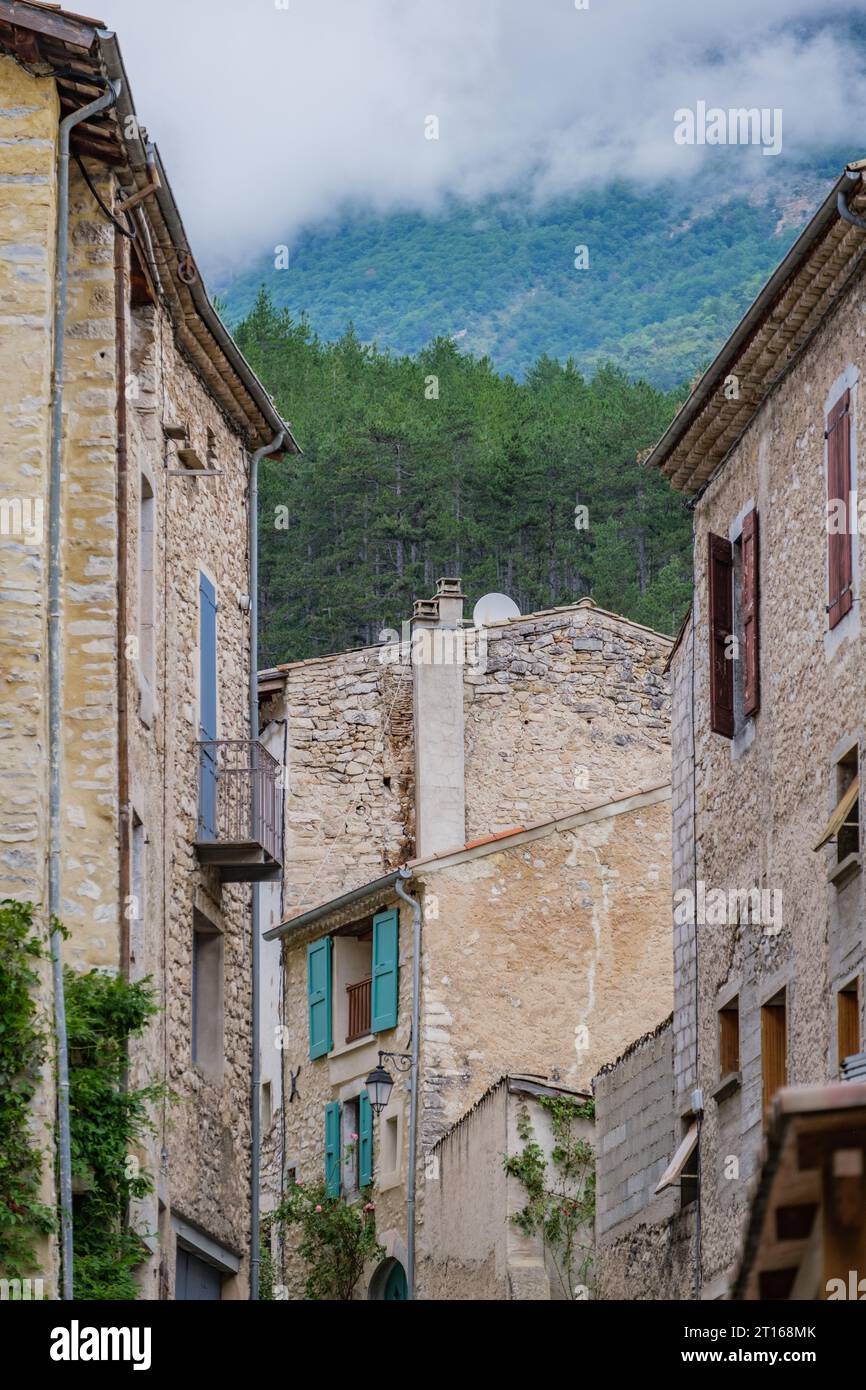 Straßen- und mittelalterliche Häuserfassaden im Dorf Chatillon en Diois mit dem verborgenen Berg hinter Wolken im Hintergrund. Stockfoto