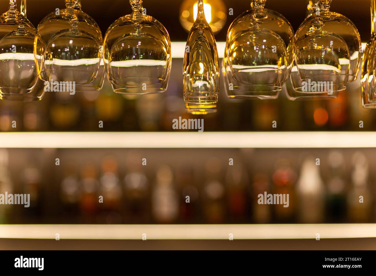 Saubere Weingläser, die über der Bar hängen, auf unscharfem Hintergrund mit Regalen mit Flaschen alkoholischer Getränke. Stockfoto