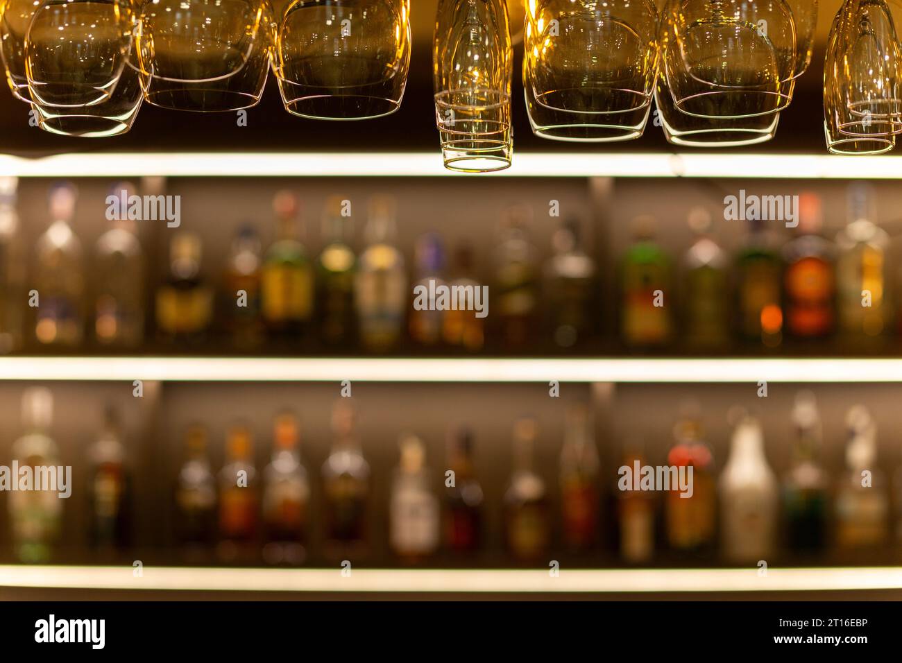 Saubere Weingläser, die über der Bar hängen, auf unscharfem Hintergrund mit Regalen mit Flaschen alkoholischer Getränke. Stockfoto