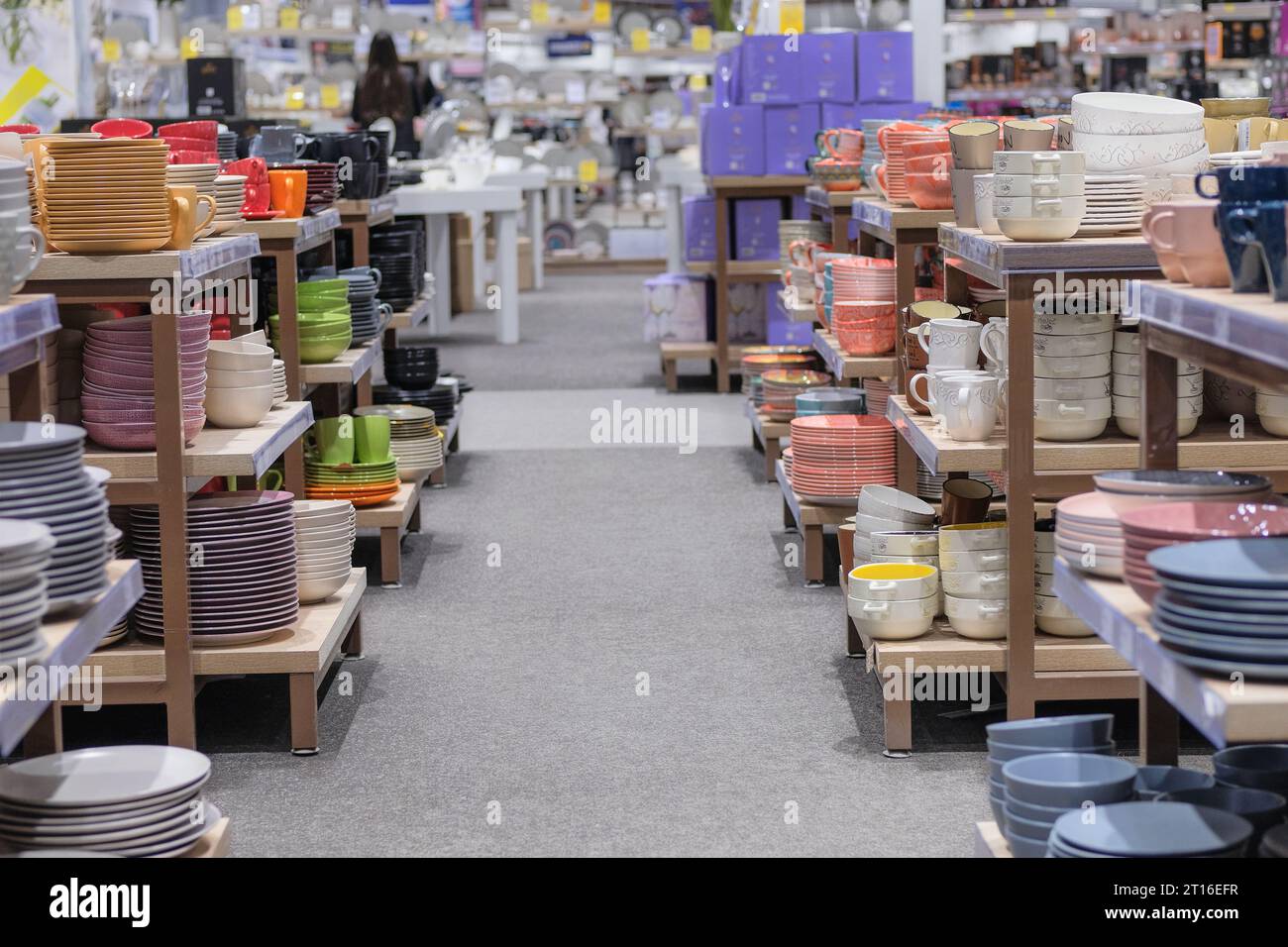 Reihen von verschiedenfarbigen Tassen, Schüsseln und Tellern für Zuhause in Regalen in einem Supermarkt. Das Geschirr wird im Laden verkauft. Stockfoto