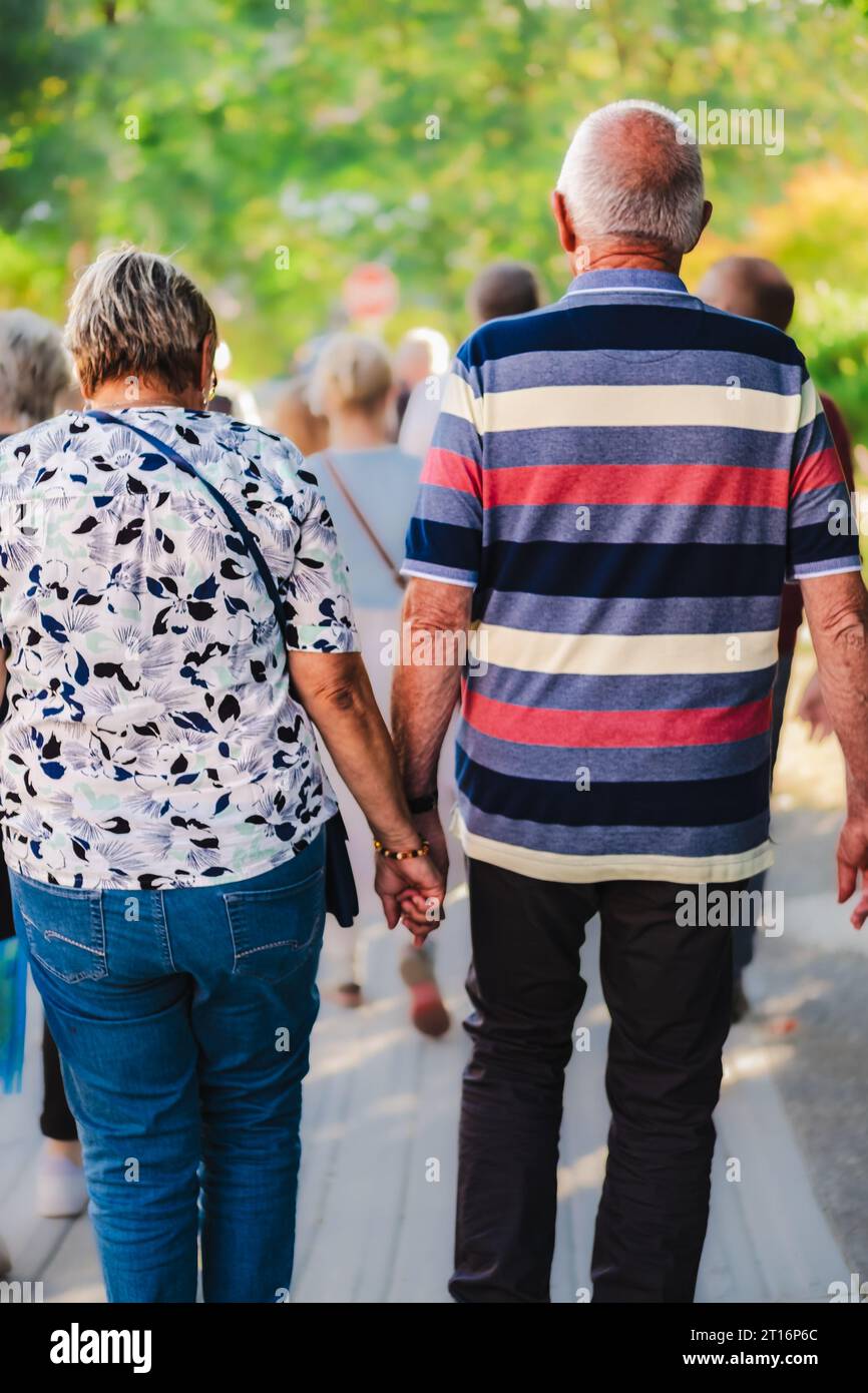 Seniorenpaar Hand in Hand im Park spazieren. Glückliches, aktives Seniorenpaar, das draußen läuft und Hände hält. Pensioniertes Paar, das Hände hält und geht Stockfoto