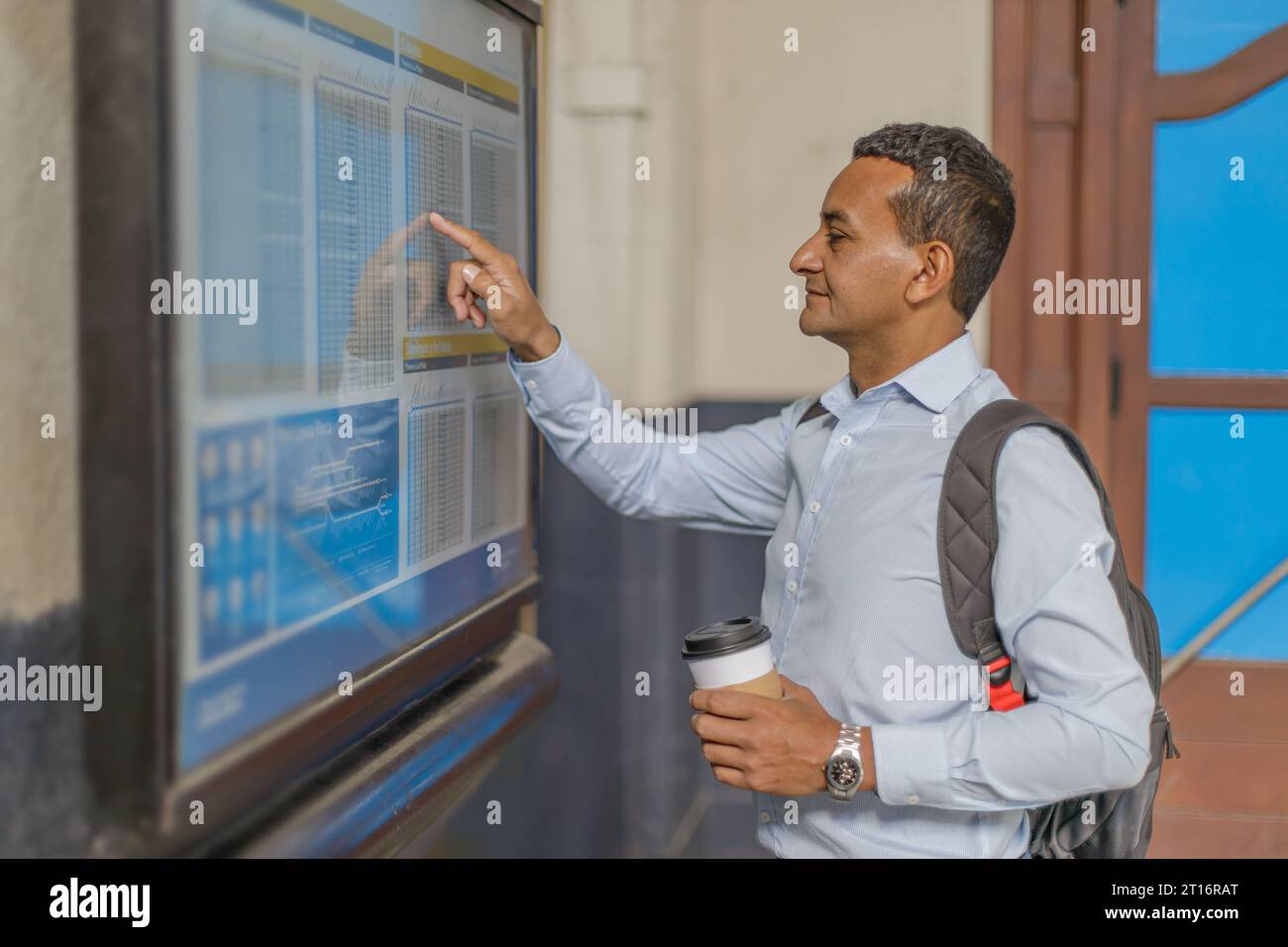 Latein-Mann, der sich Werbetafeln mit Zugfahrplänen ansieht. Stockfoto