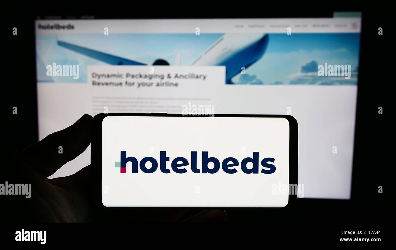 Person mit Smartphone und Logo des Reisetechnologieunternehmens Hotelbeds Group S.L.U. vor der Website. Schwerpunkt auf dem Display des Telefons. Stockfoto