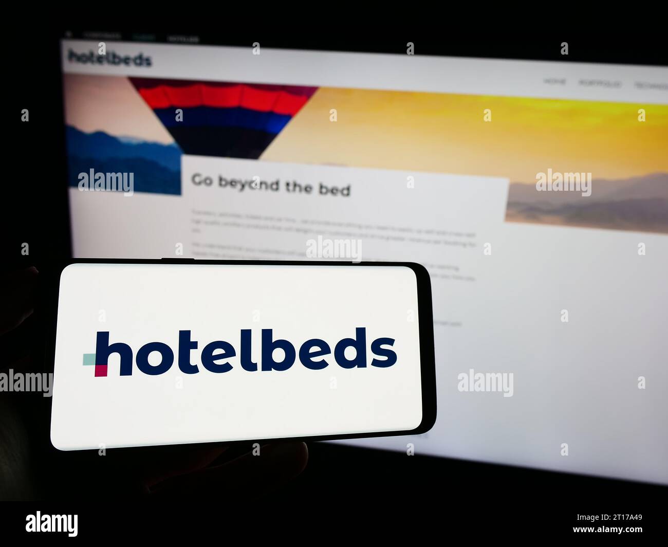 Person, die ein Mobiltelefon mit dem Logo des Reiseunternehmen Hotelbeds Group SLU vor der Business-Webseite hält. Schwerpunkt auf dem Display des Telefons. Stockfoto