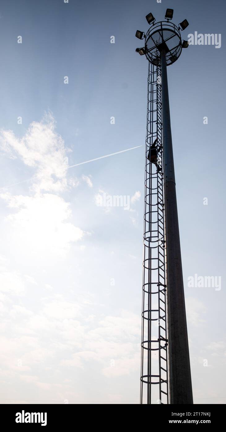 Siluethe des Arbeiters, der auf den Turm des Hochhauses des Kraftwerks vor einem bewölkten blauen Himmel klettert Stockfoto