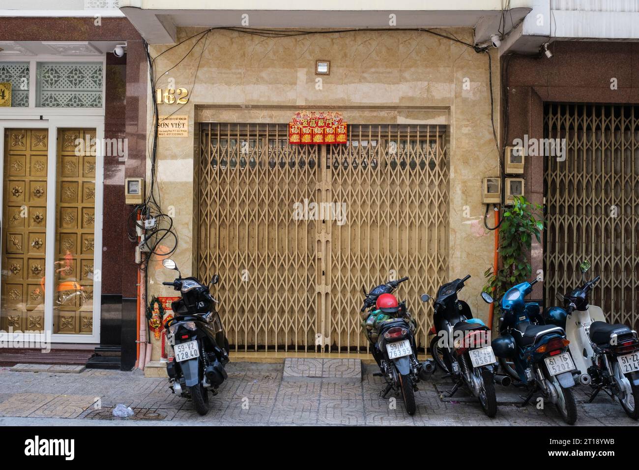 Der kleine Spiegel über der Tür verschreckt Dämonen aus dem Haus. Ho Chi Minh, Vietnam. Ein rot-goldenes Banner verkündet Glück und Glück. Stockfoto