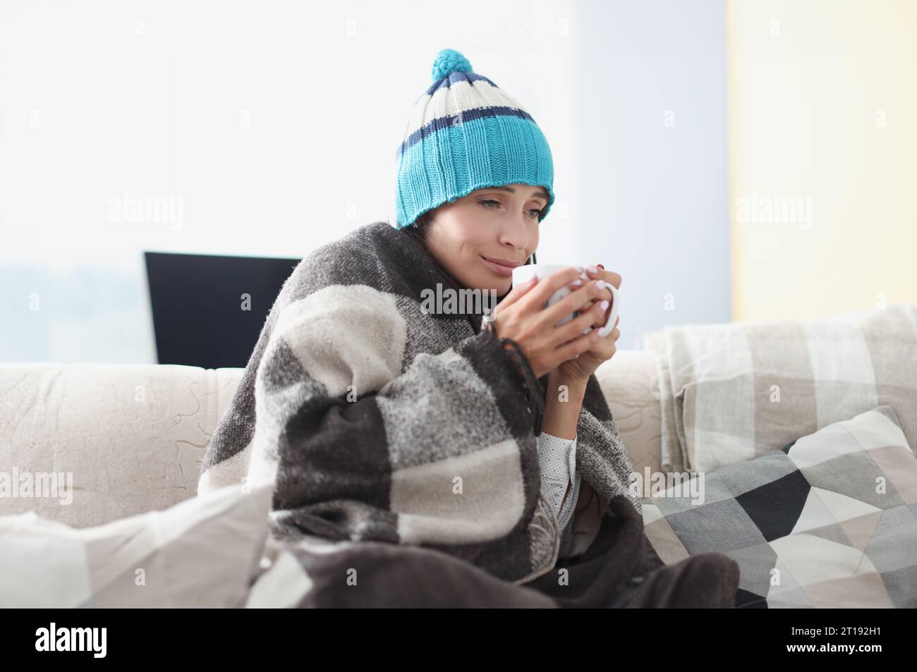 Gekühlte Frau auf der Couch in Decke und Hut hält heiß becher Stockfoto Gekühlte Frau auf der Couch in Decke und Hut hält heiß becher Stockfoto