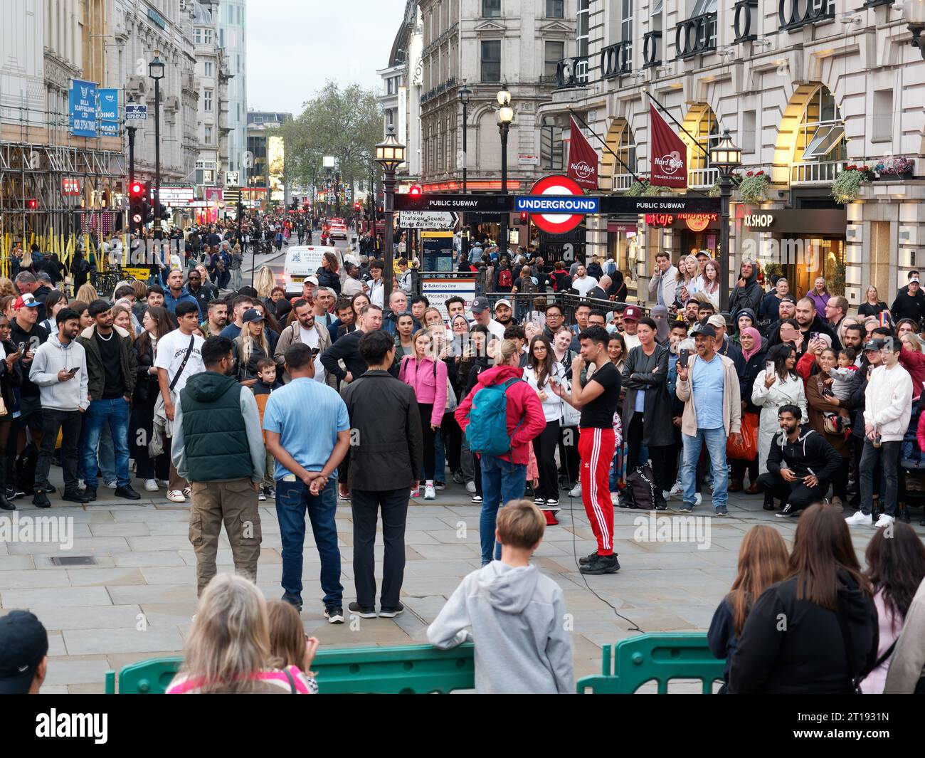 Ein Straßenkünstler unterhält eine Menschenmenge, meist Touristen, im Piccadilly Circus London Stockfoto