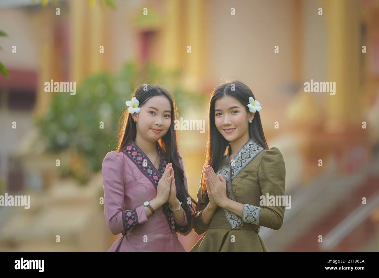 Zwei junge Frauen in traditioneller laotischer Kleidung mit Händen in Gebetsposition Stockfoto