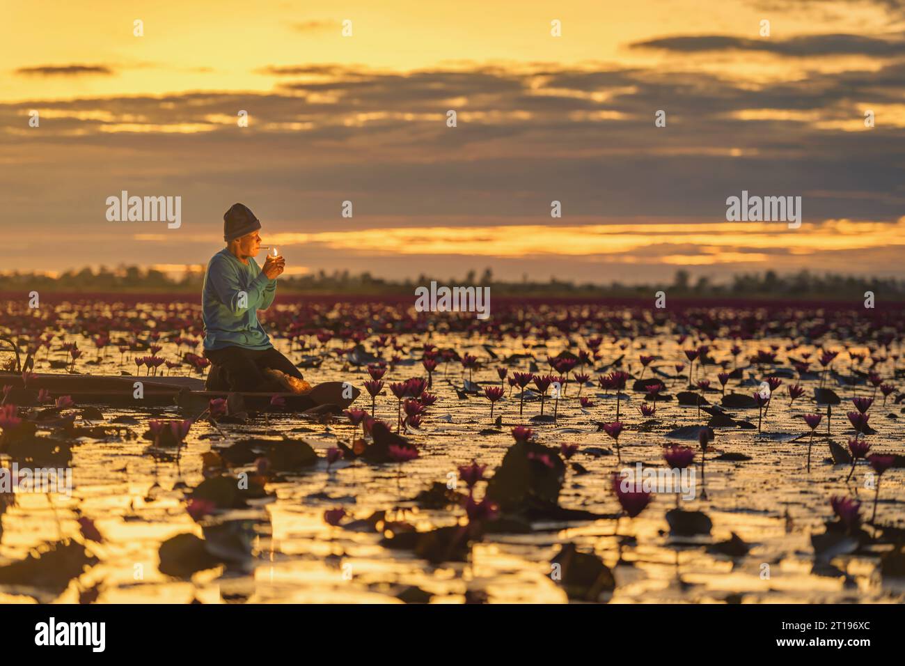 Fischer, der in einem Boot sitzt und bei Sonnenuntergang eine Zigarette raucht, Red Lotus Sea (Talay Bua Daeng), Udon Thani, Thailand Stockfoto